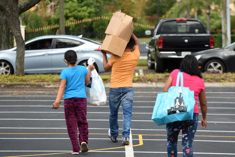 A families carrying boxes and bags walk away from a food distribution center in Florida.