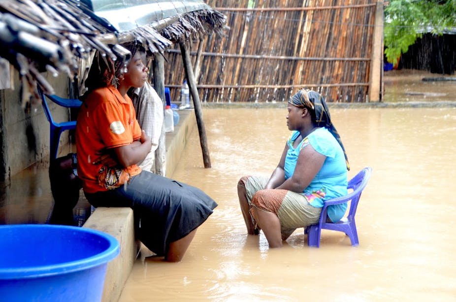 Two women sit in a flooded yard