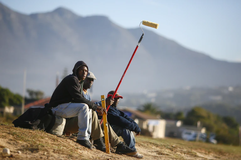 Three men seek work by the side of the road. One carries a spirit level and the other a roller paint brush on a long stick.