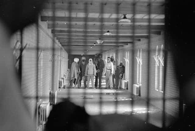 Prisoners wearing cloaks and football helmets stand behind bars as they begin negotiations with New York State officials in 1971's Attica standoff.