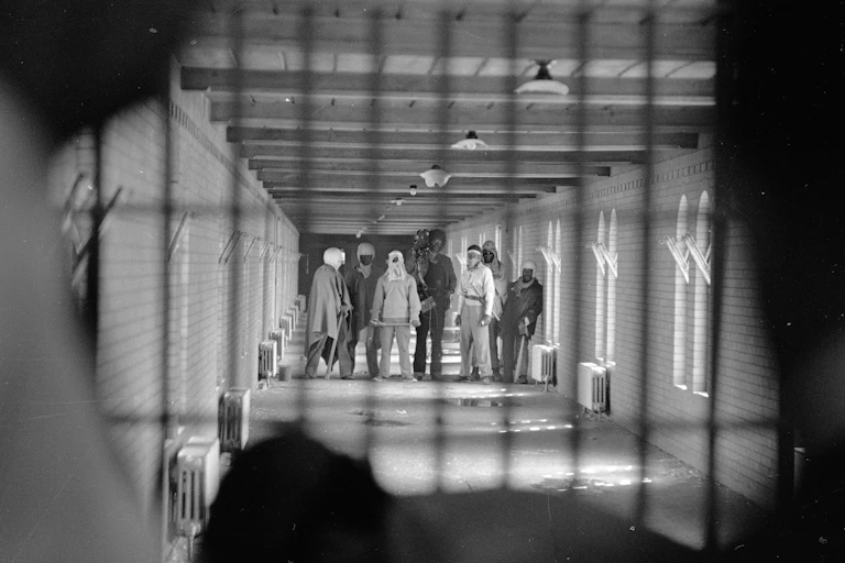 Prisoners wearing cloaks and football helmets stand behind bars as they begin negotiations with New York State officials in 1971's Attica standoff.