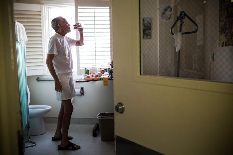 A prisoner sips water as he stands in a room at the hospice wing of California Medical Facility.