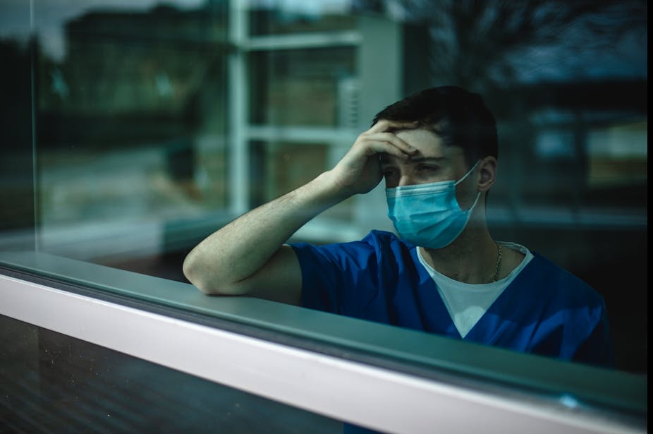 masked male nurse holding head and looking out window