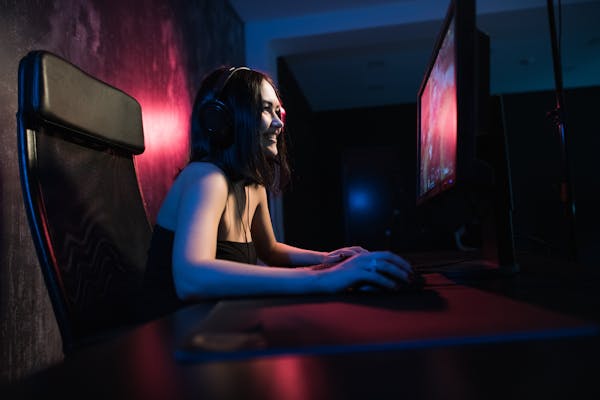 A young woman sits in front of a computer gaming set up.