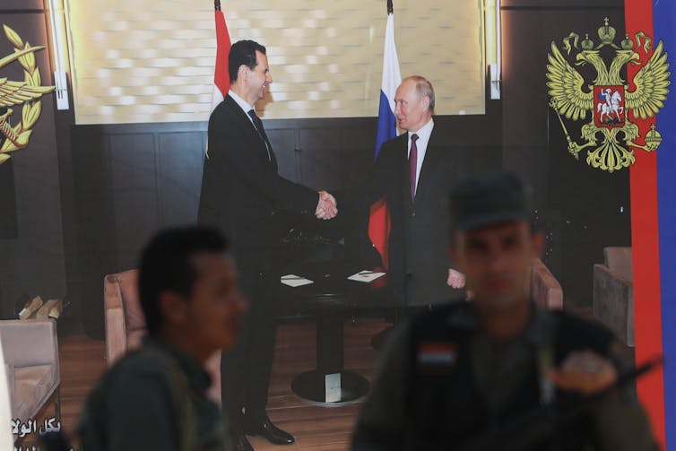 Syrian policemen stand guard in front of poster of Syrian President Bashar Assad and Russian President Vladimir Putin