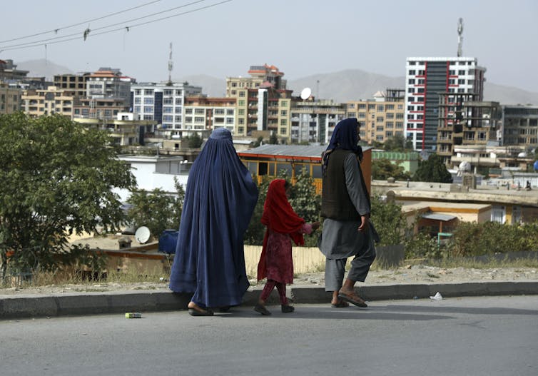 Afghan people walk on a street in Kabul with high-rises in the background.