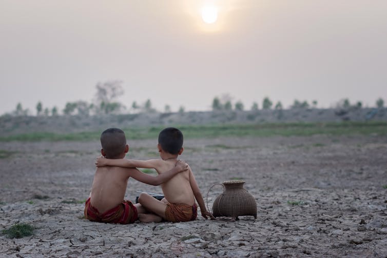 two boys with arms around each other on cracked earth