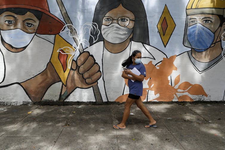 Woman walking outside a large mural of Filipino people in masks.