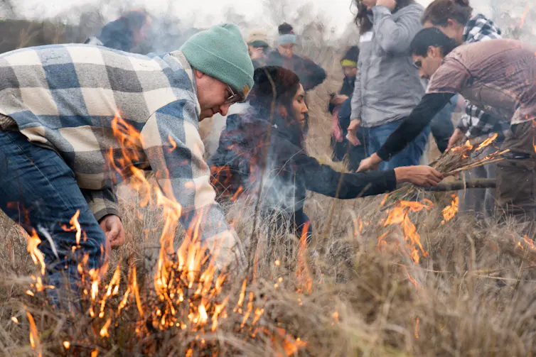 People wearing jackets against the cool weather light small, controlled fires in grasslands