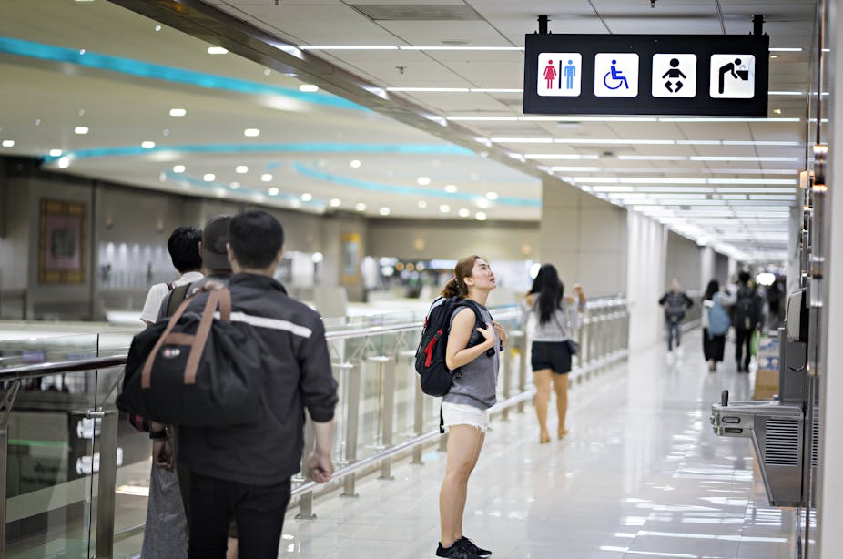 A woman looks at a toilet sign in an airport.