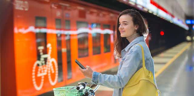 Young woman with bicycle holding mobile phone while standing on train platform.