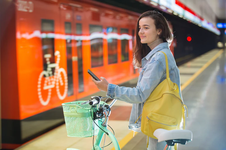 Young woman with bicycle holding mobile phone while standing on train platform.
