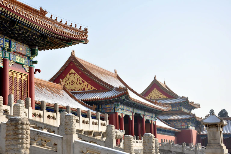 Traditional Chinese buildings with snow on their sloped, red roofs.