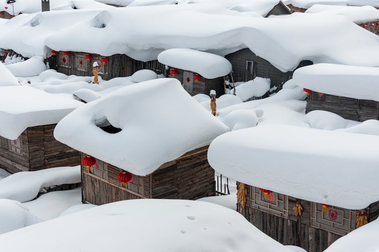 Small wooden buildings topped with thick snow.