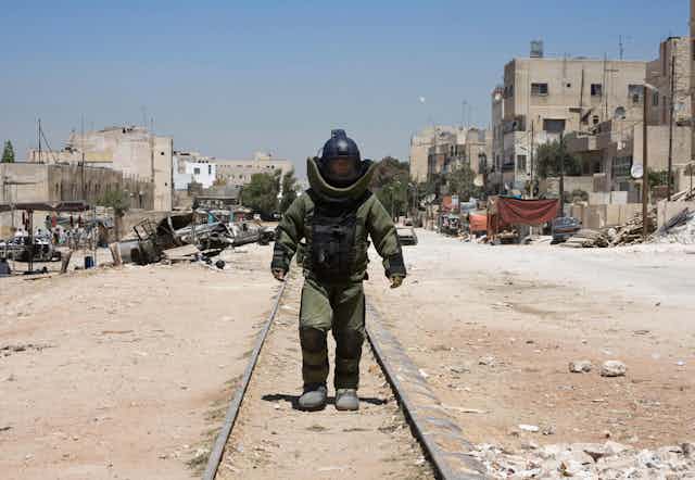 Man in bomb disposal suit walking down train track.