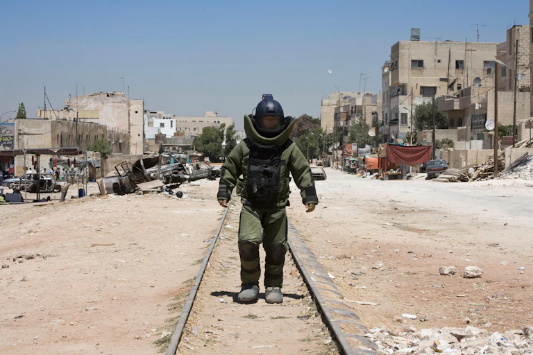 Man in bomb disposal suit walking down train track.