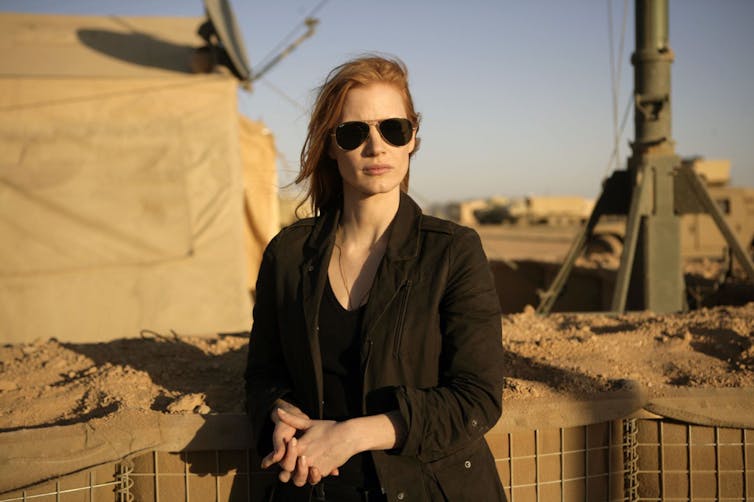 Woman dressed in black against military base backdrop.