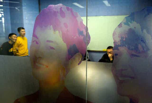 Images of two young male faces on a glass wall.