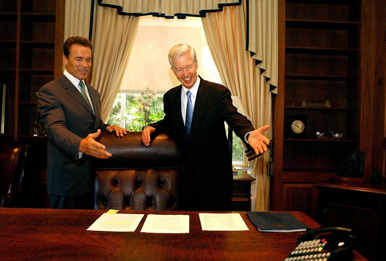 Gov.-election Arnold Schwarzenegger and Governor Gray Davis standing behind Davis' desk at the state Capitol.