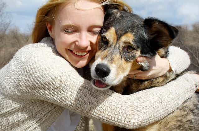 A smiling woman lovingly wraps her arms around a large dog