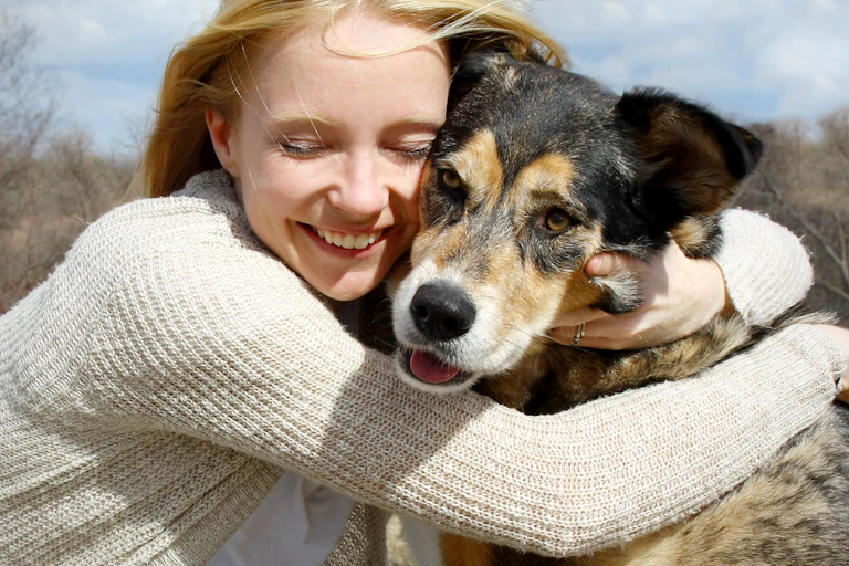 A smiling woman lovingly wraps her arms around a large dog