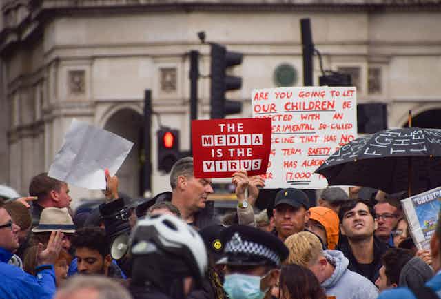 A man at a protest holding up a sign that reads 'the media is the virus'