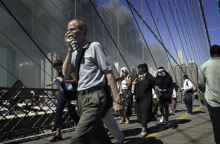 Un homme portant un mouchoir sur sa bouche traverse le pont de Brooklyn avec d’autres personnes