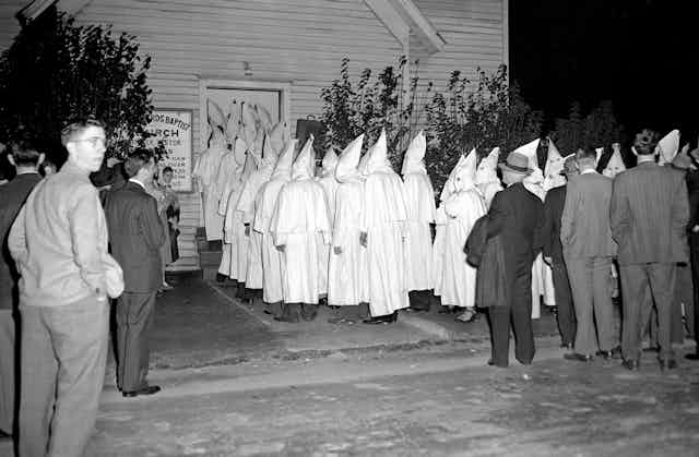 Members of the Ku Klux Klan in traditional white hoods and robes enters a Baptist church.