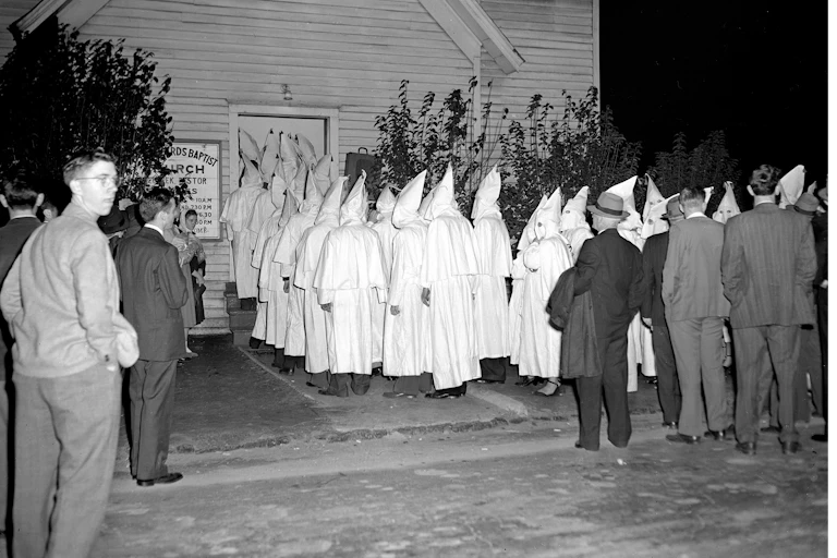 Members of the Ku Klux Klan in traditional white hoods and robes enters a Baptist church.