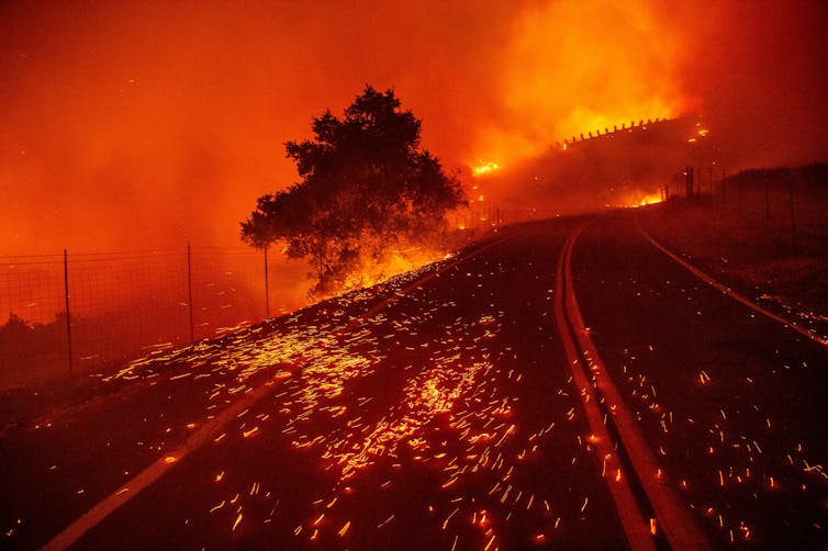 Burning embers on a road with a fire in a home far in the background.