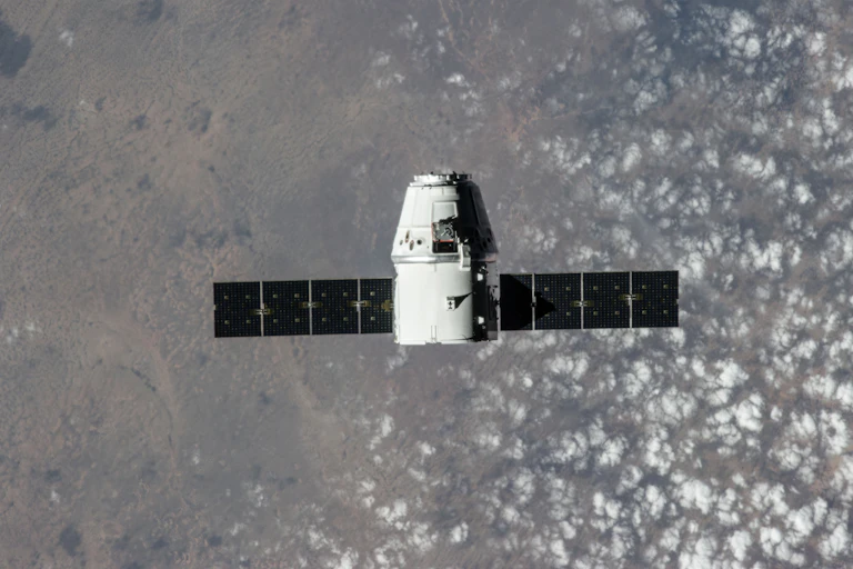 A small white cylindrical capsule floating with the Earth in the background.