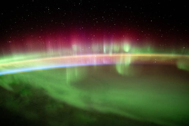 Colorful green and pink hues in the atmosphere of Earth with the blackness of space in the background.