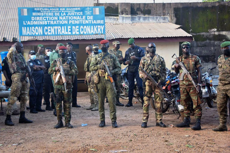 Men in camouflage uniform, carrying weapons, stand in the street