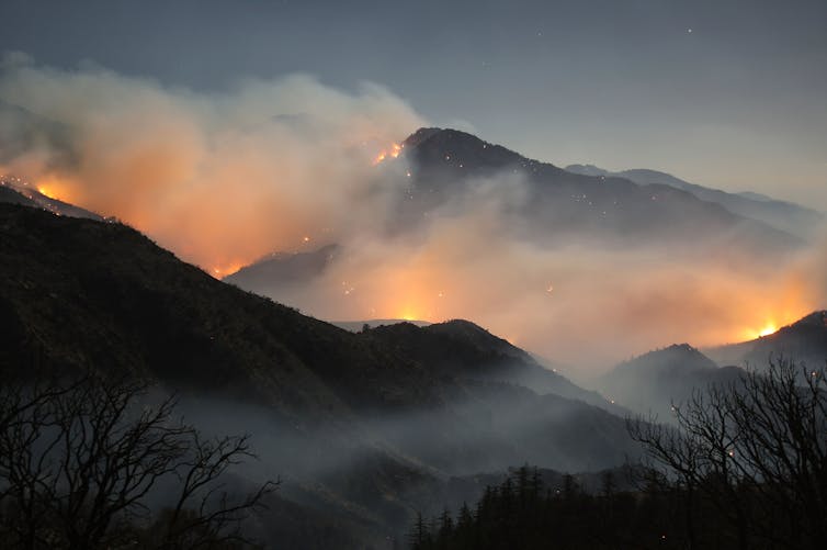 A fire roars though a mountain range at night.
