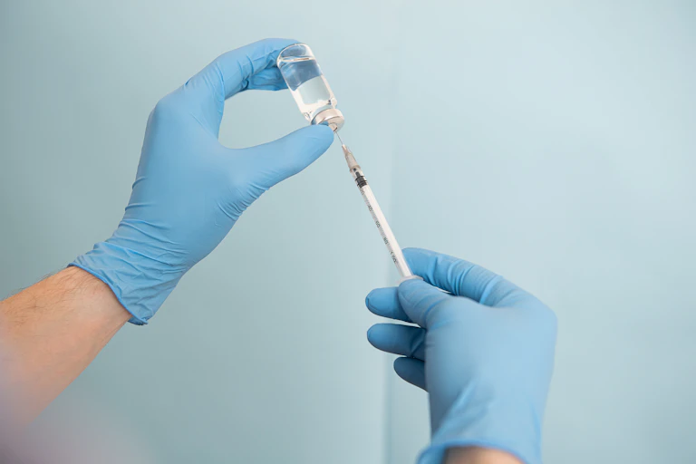 Doctor wearing blue surgical gloves holds a vial and a needle in the air.