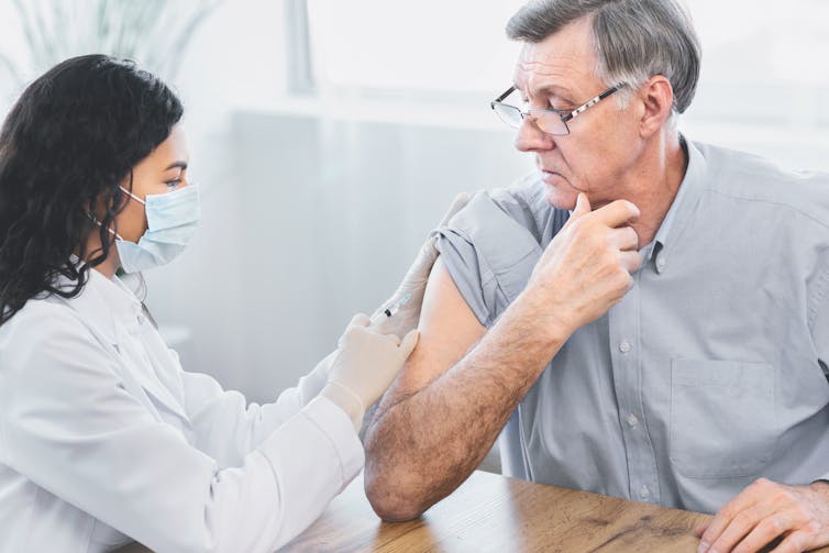 Female doctor gives elderly patient an injection into his arm.