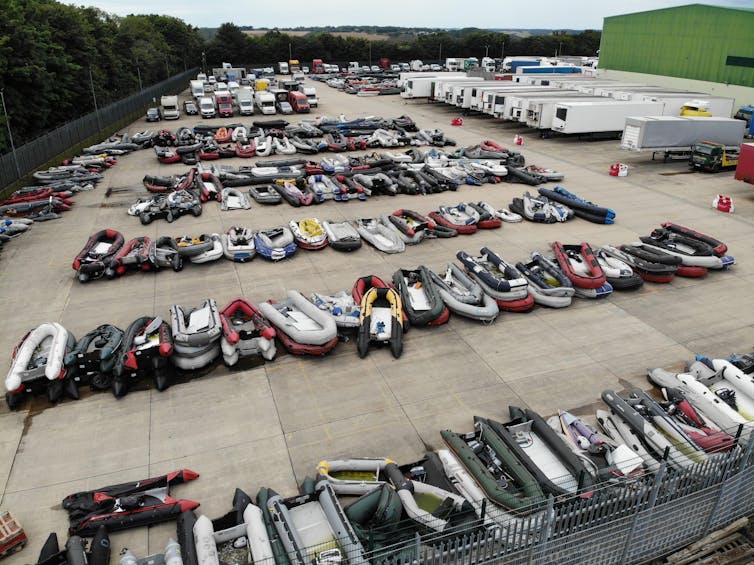 Rows of small migrant boats stacked in a lot at a holding facility.