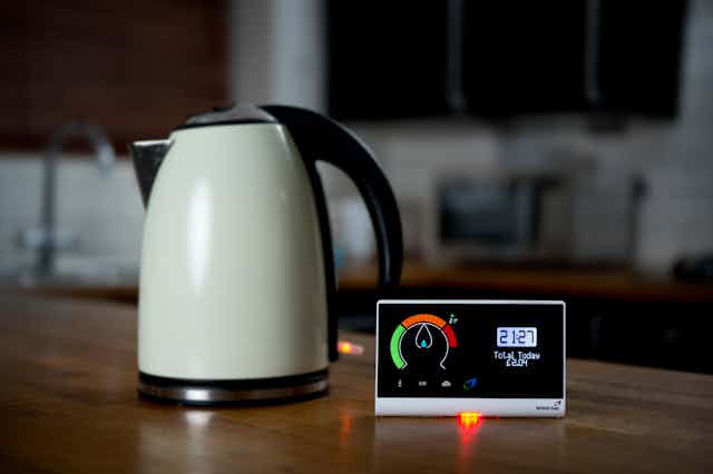 A white kettle on a kitchen table top next to a smart metre.
