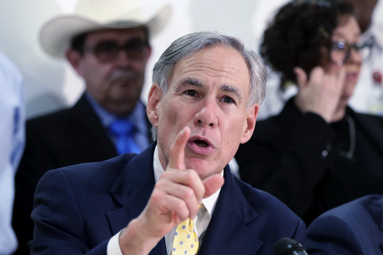 Texas Gov. Greg Abbott in a blue blazer and yellow tie, gesturing with his right hand.