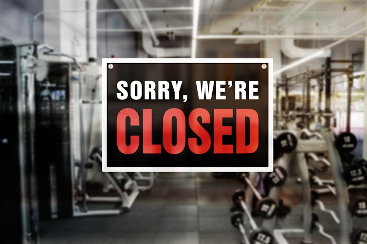 A sign reads 'Sorry, we're closed' on the window of a workout room