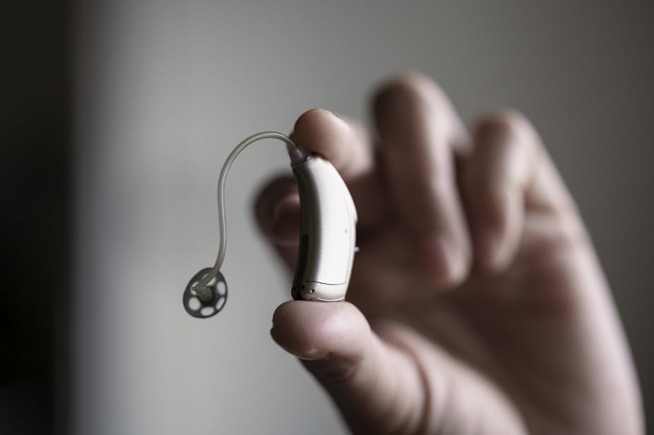 Hand holding hearing aid between two fingers.
