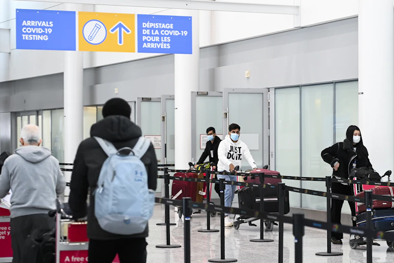 Travellers with luggage in an airport terminal under a sign directing them towards COVID-19 testing