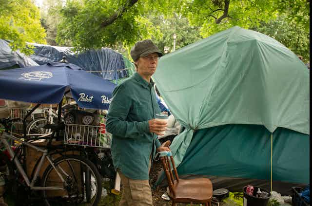 A women stands holding a coffee in a homeless tent encampment