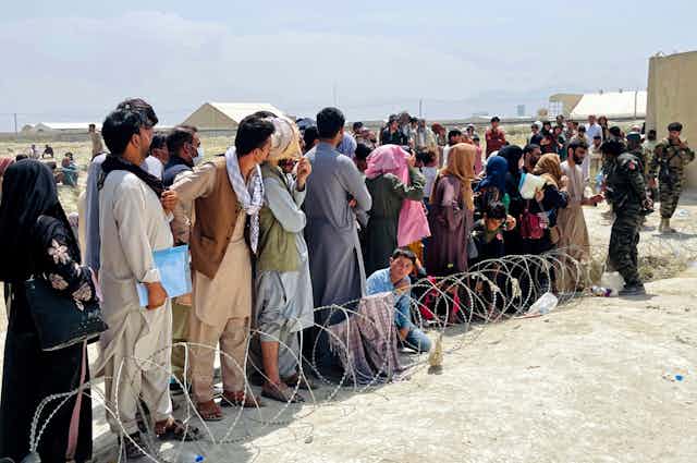 A line of Afghans next to barbed wire standing in the sun outside the airport in Kabul.