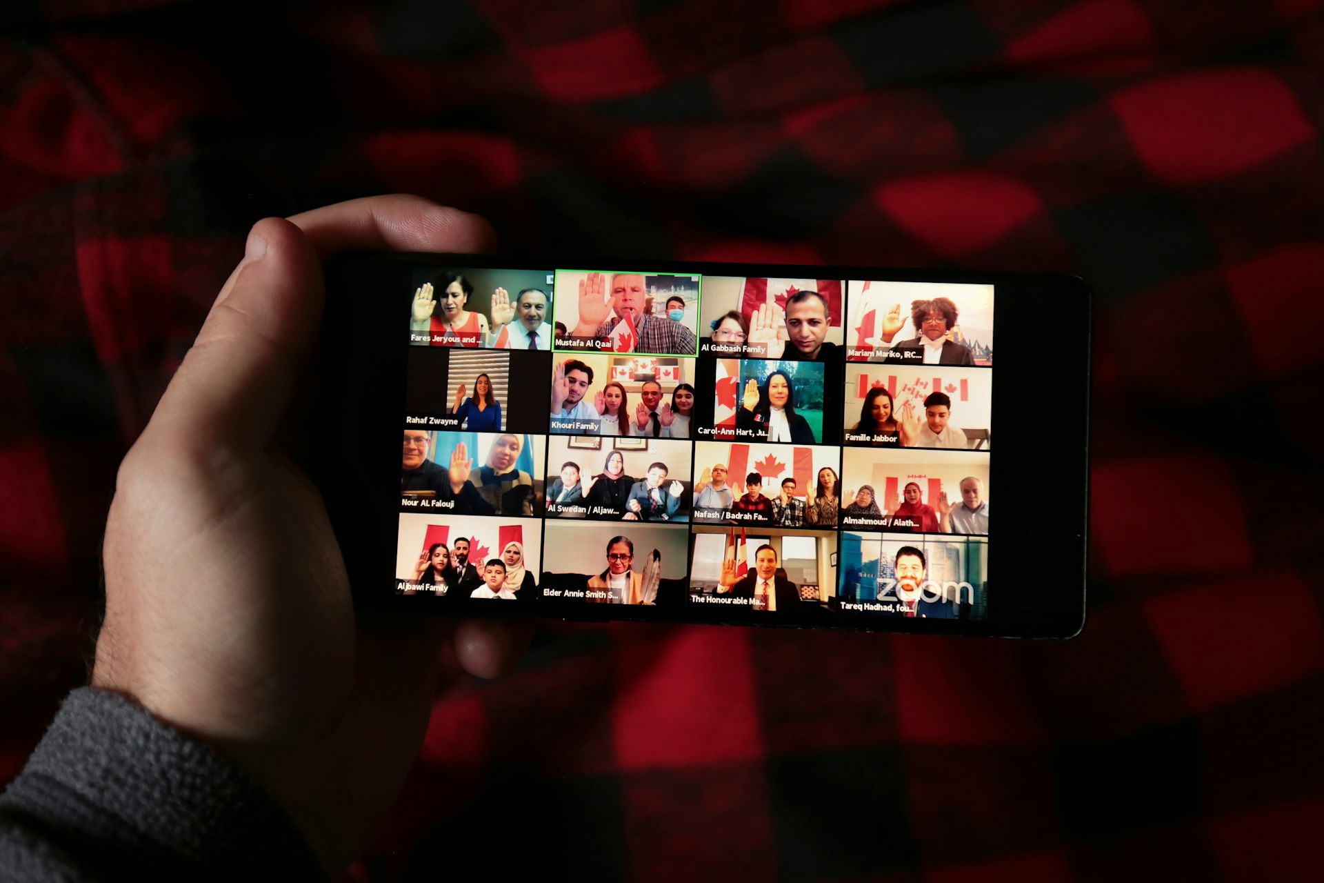 A man holds up a phone that shows a screen of many people taking part in the citizenship ceremony.