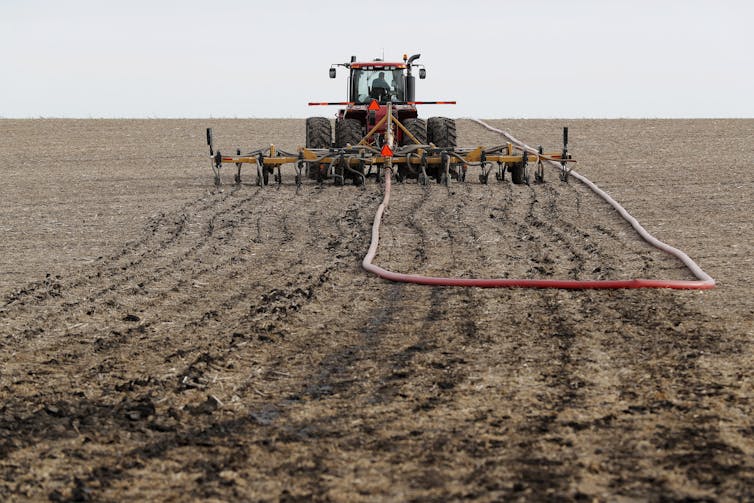 A tractor spreads manure on a dirt field.
