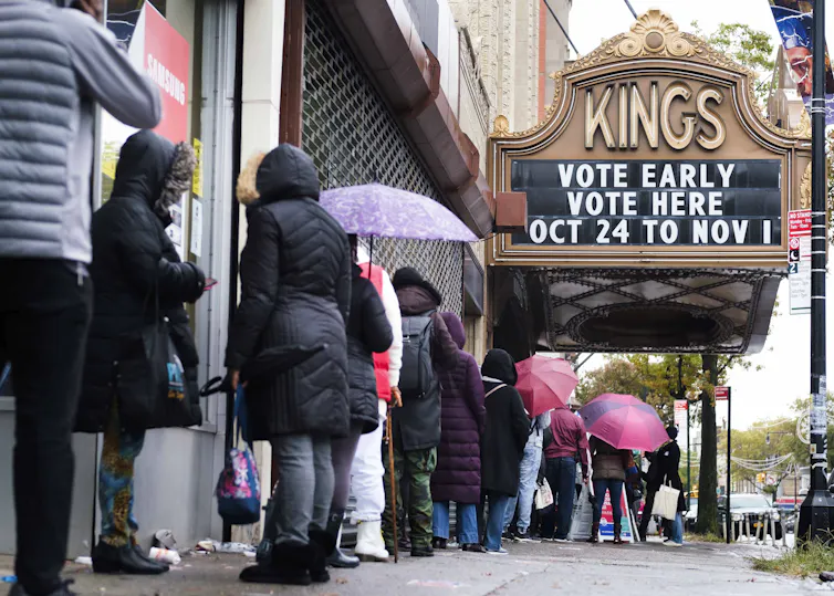 A line of people waiting to enter a theatre-turned-polling-station with a sign reading 'vote early, vote here'.
