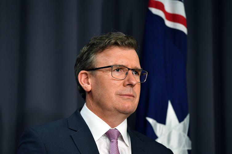Government minister in suit and tie standing in front of Australian flag