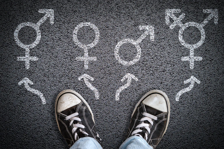 a person's feet in sneakers standing on asphalt road with gender symbols of male, female, bigender and transgender.