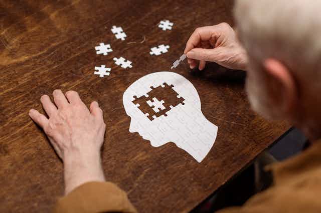 Señor mayor haciendo un puzzle con forma de cabeza humana.